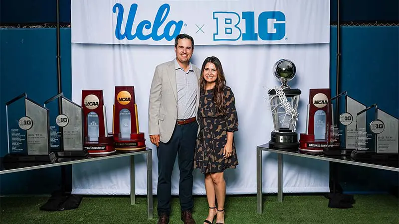 A man and woman posing for a picture with a 'UCLA x B1G' banner behind them