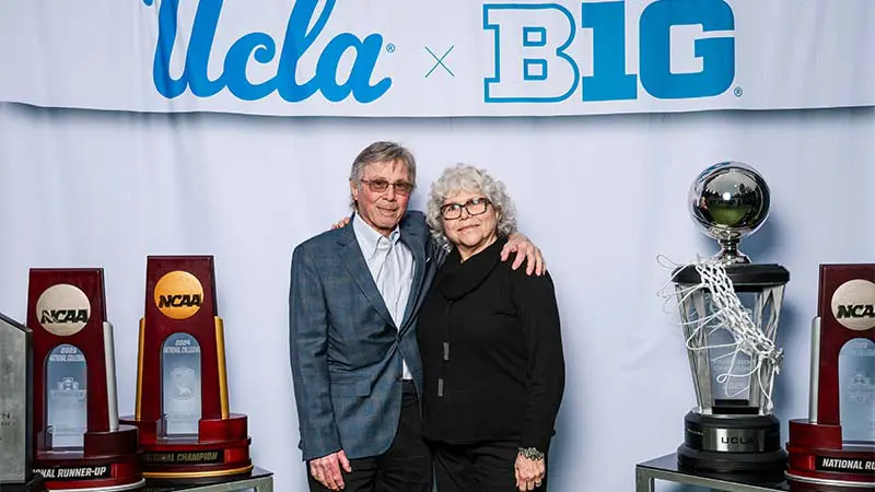 A man and woman posing for a picture with a 'UCLA x B1G' banner behind them