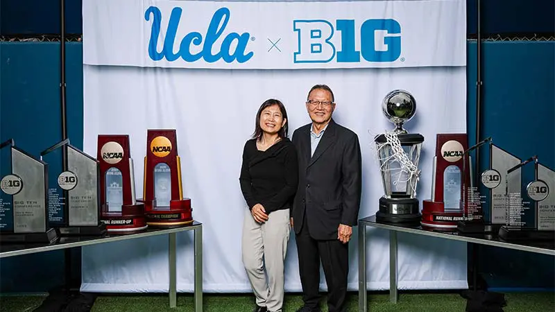 A man and woman posing for a picture with a 'UCLA x B1G' banner behind them